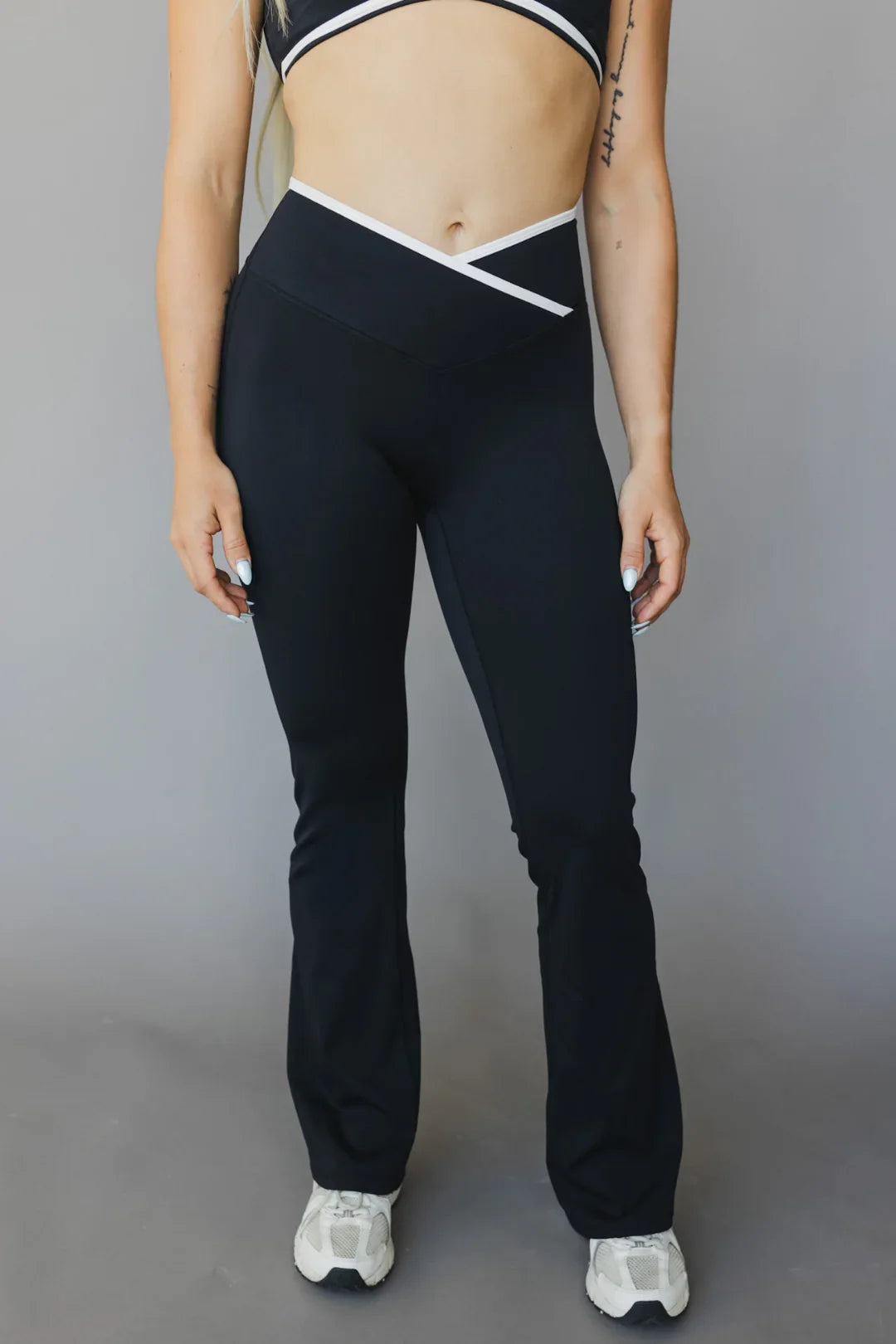 Woman wearing black high-waisted flare leggings and sports bra with white trim