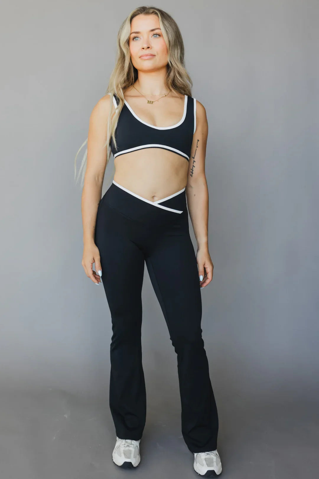 Woman modeling black V-waist flare yoga pants and sports bra with white trim on gray background