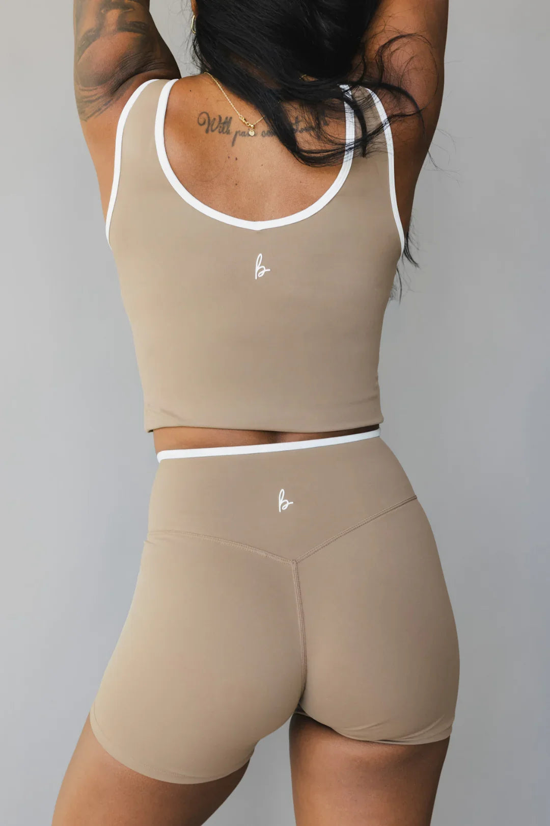 Woman modeling beige workout shorts and crop top set with white trim and logo on back