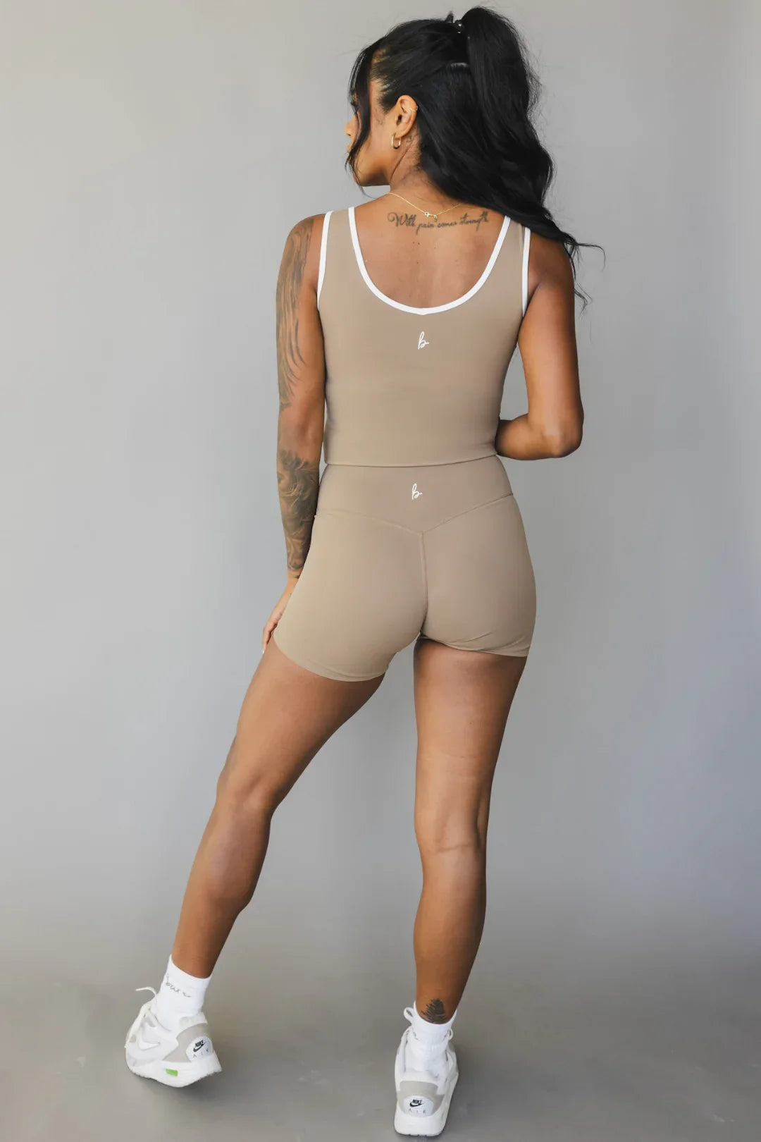 Woman in tan athletic shorts and tank top with white trim, standing against gray backdrop