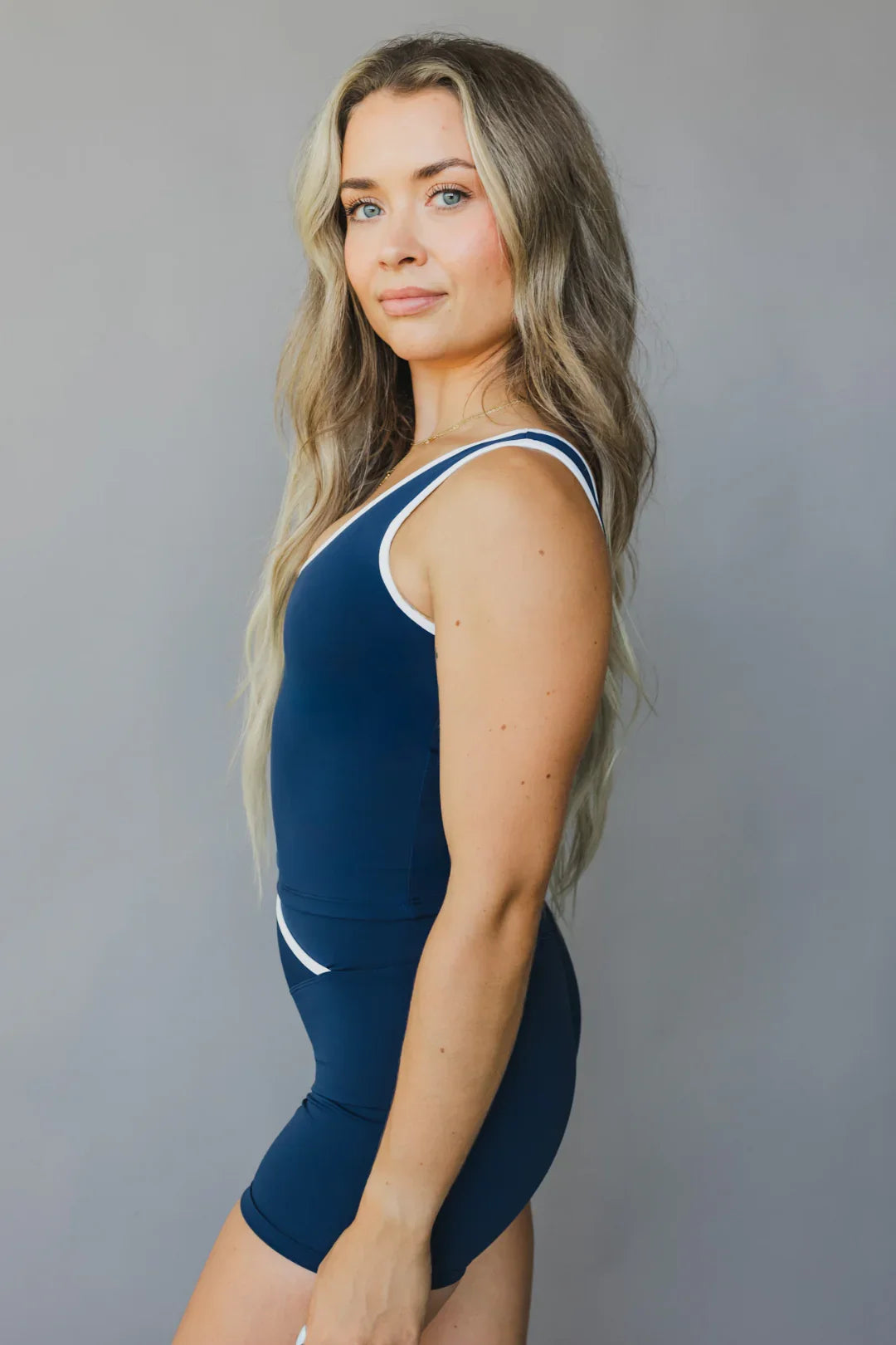 Woman in blue athletic bodysuit with white trim posing against plain gray background