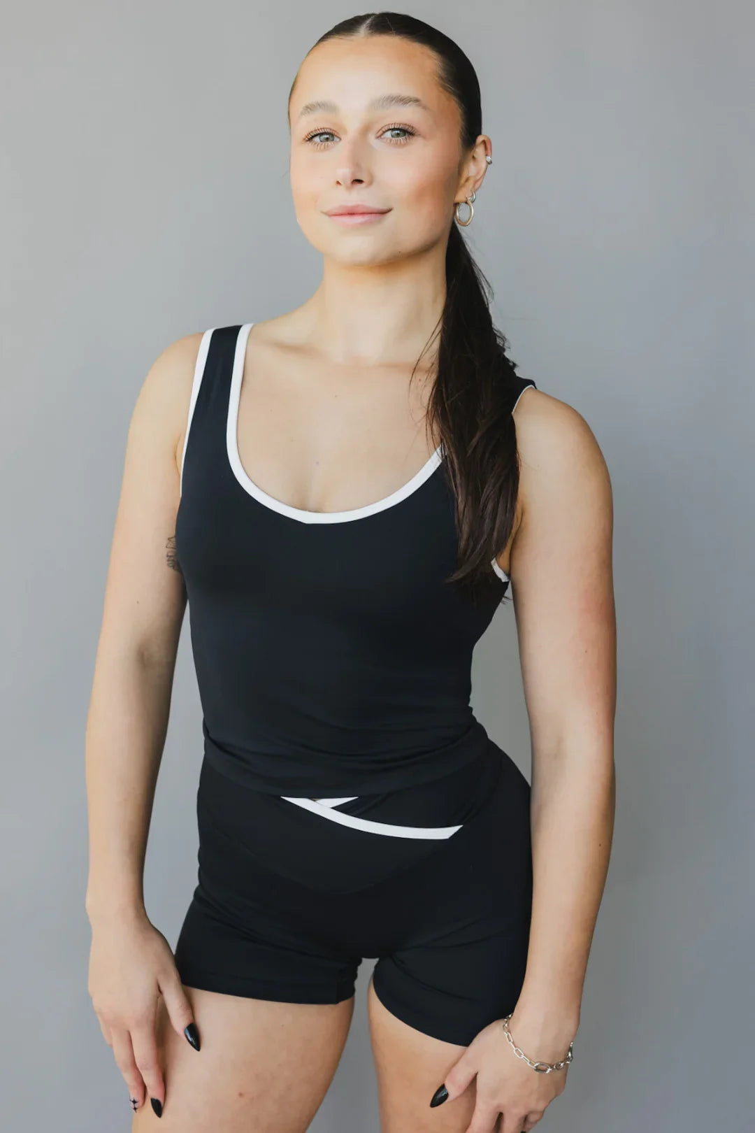 Woman in black and white athletic tank top and shorts posing against gray background