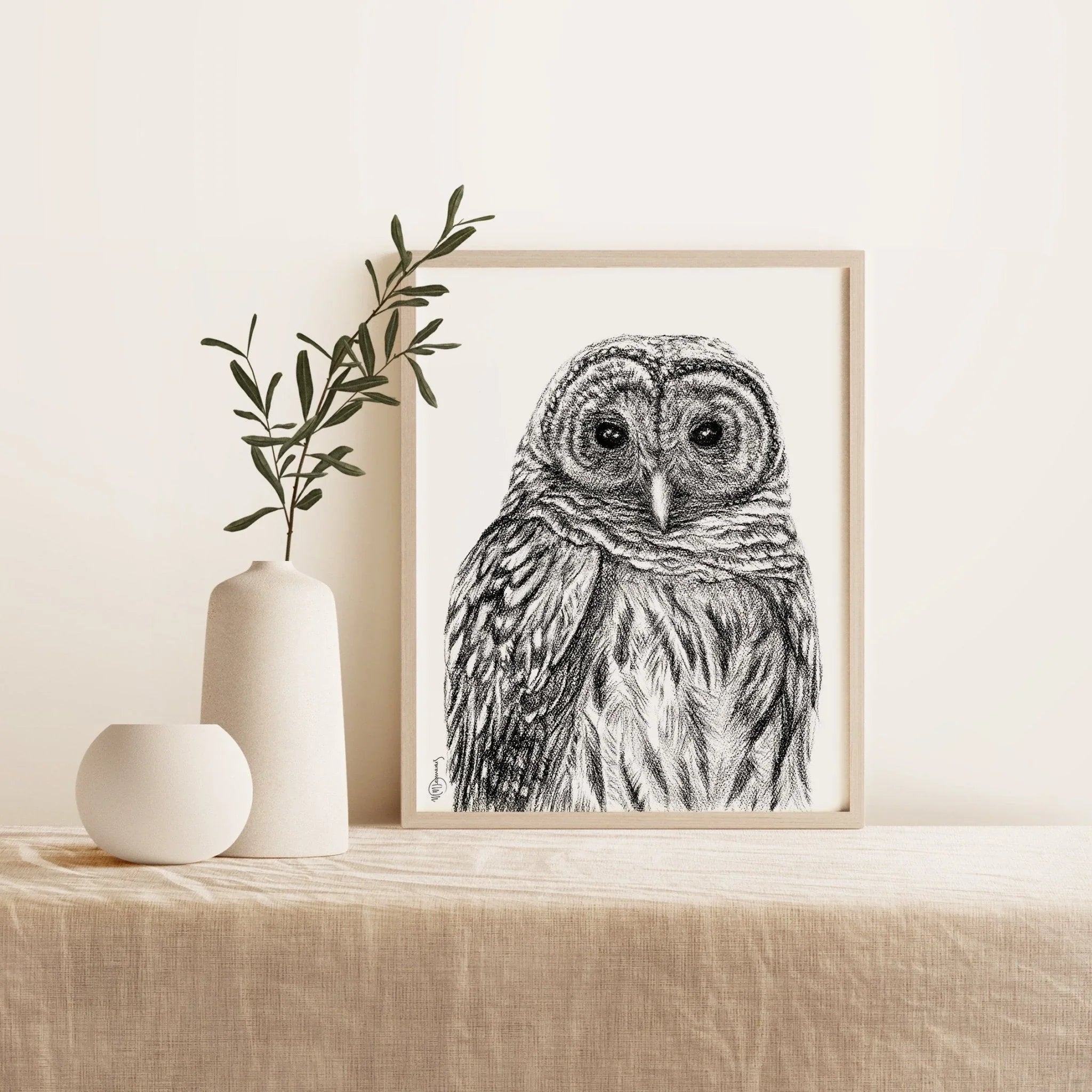Barred owl black and white art print in wooden frame on beige linen table with ceramic vases.