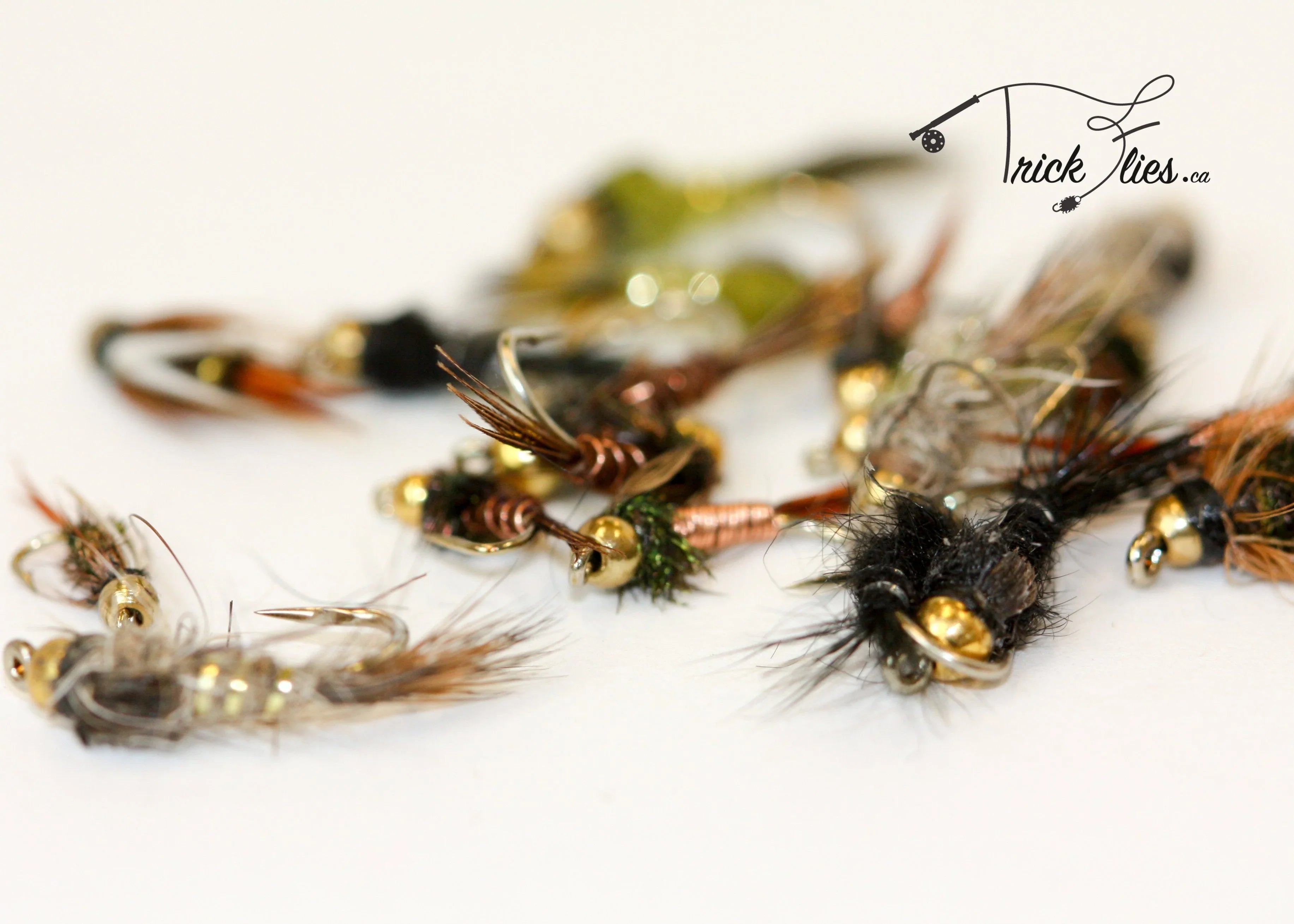 Assorted nymph fishing flies with bead heads on a white background, Trick Flies branding visible