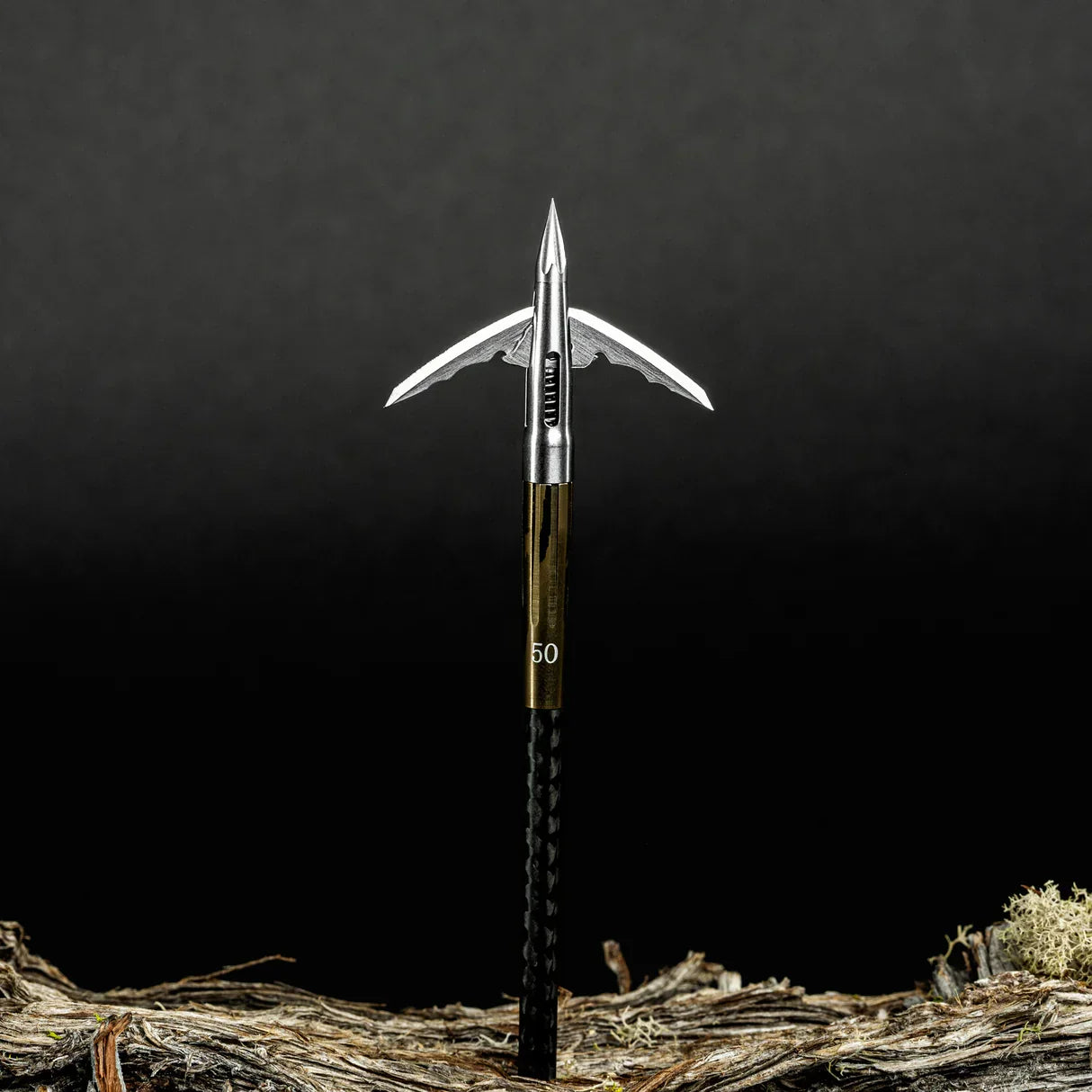 Broadhead arrow tip with sharp stainless steel blades on a black shaft, outdoor setting