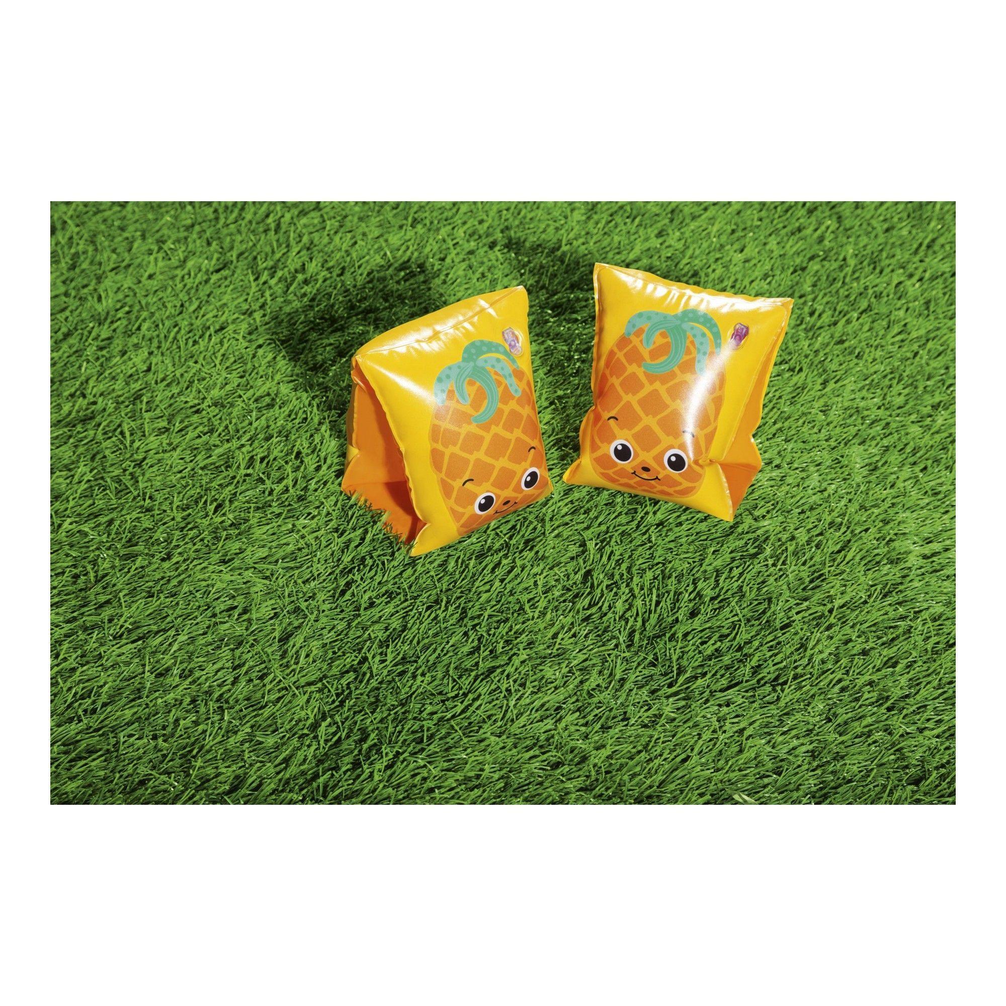 Pair of yellow pineapple floaties with cartoon faces on green grass