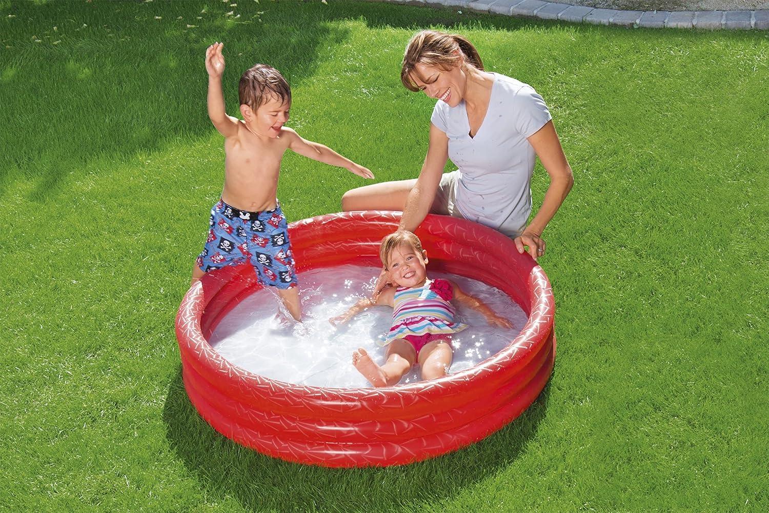 Kids and woman playing in red inflatable kiddie pool on grass lawn outdoors