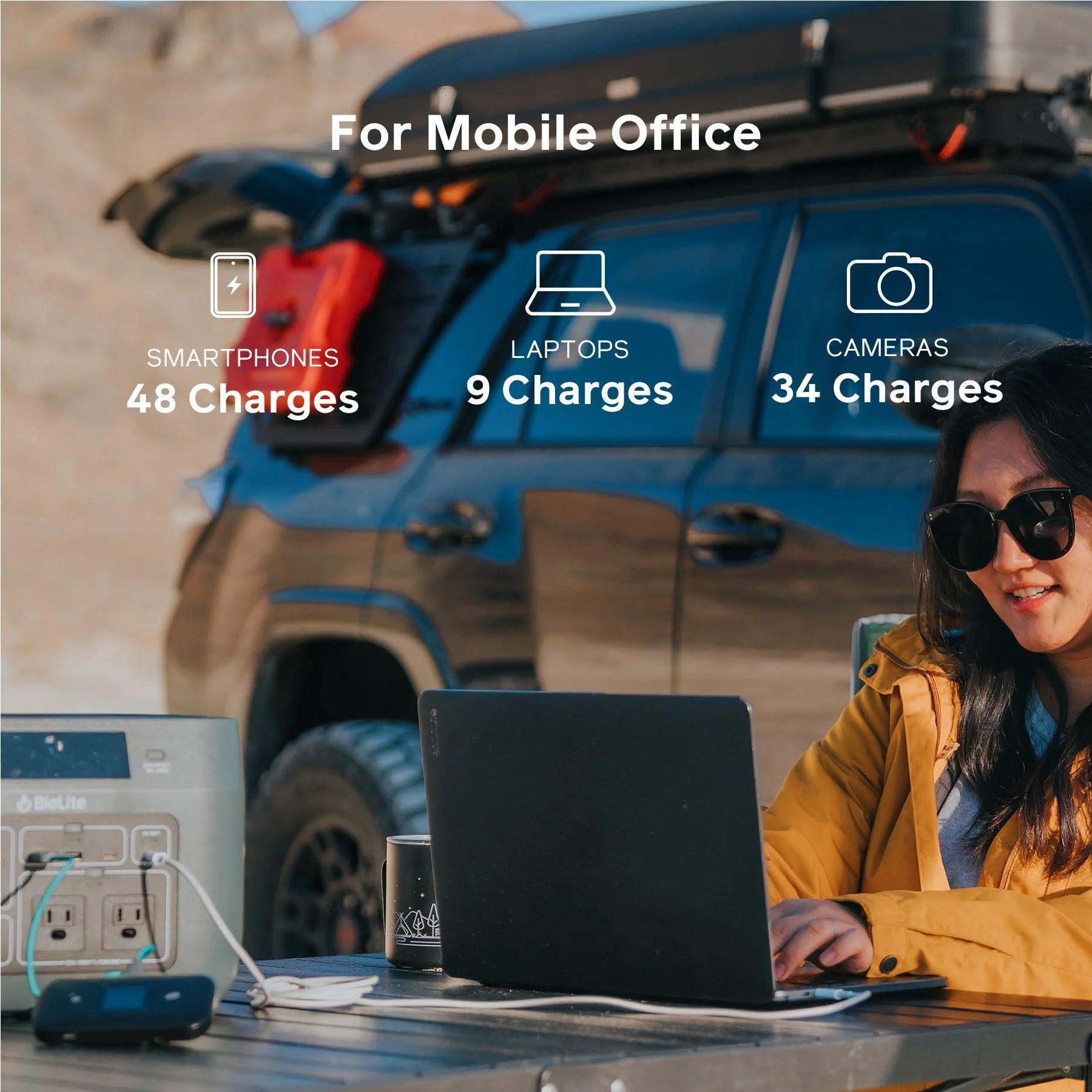 Woman using a laptop outdoors with BioLite BaseCharge 600 power station by SUV, mobile office setup