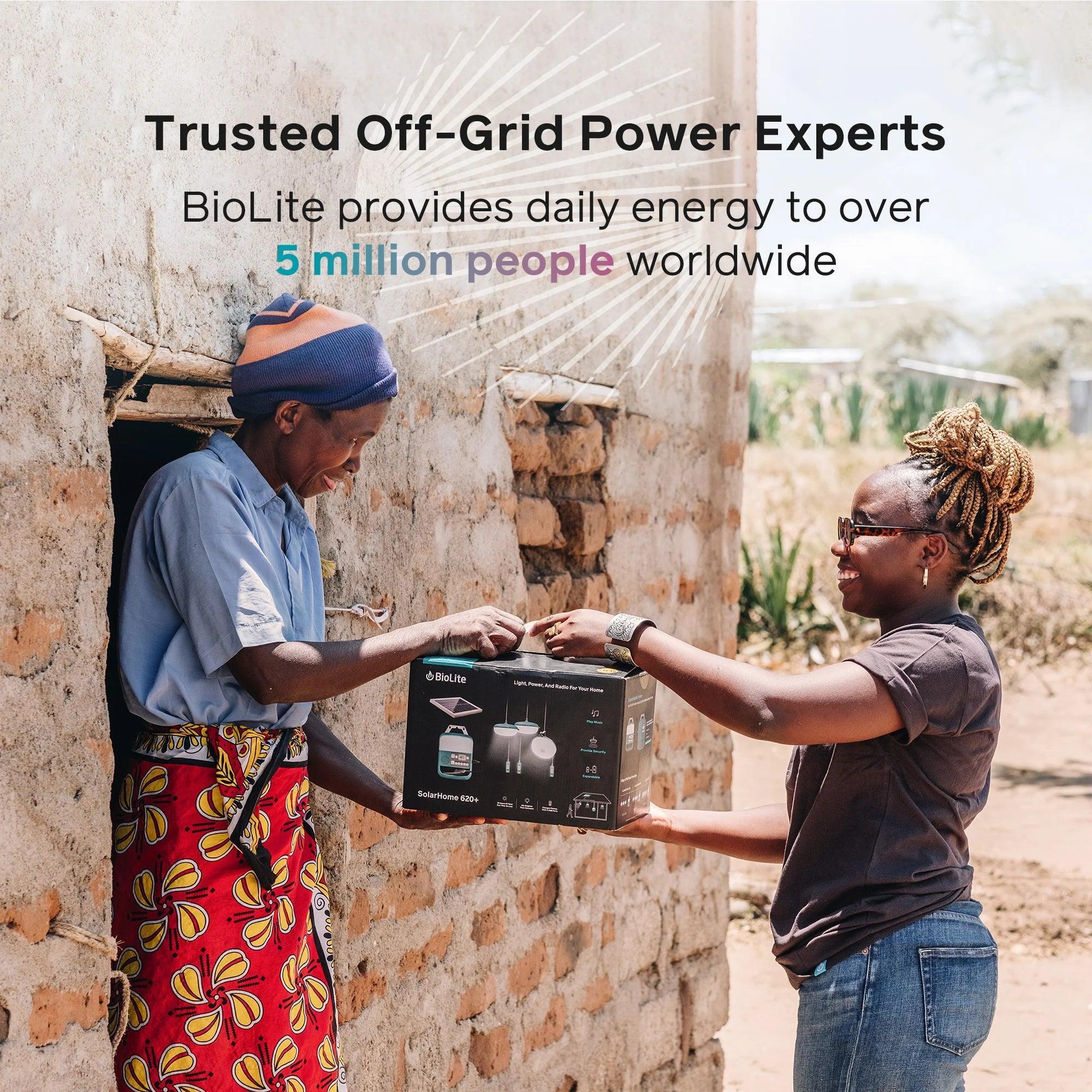 Woman handing BioLite SolarHome 620 box to another woman outside brick rural house