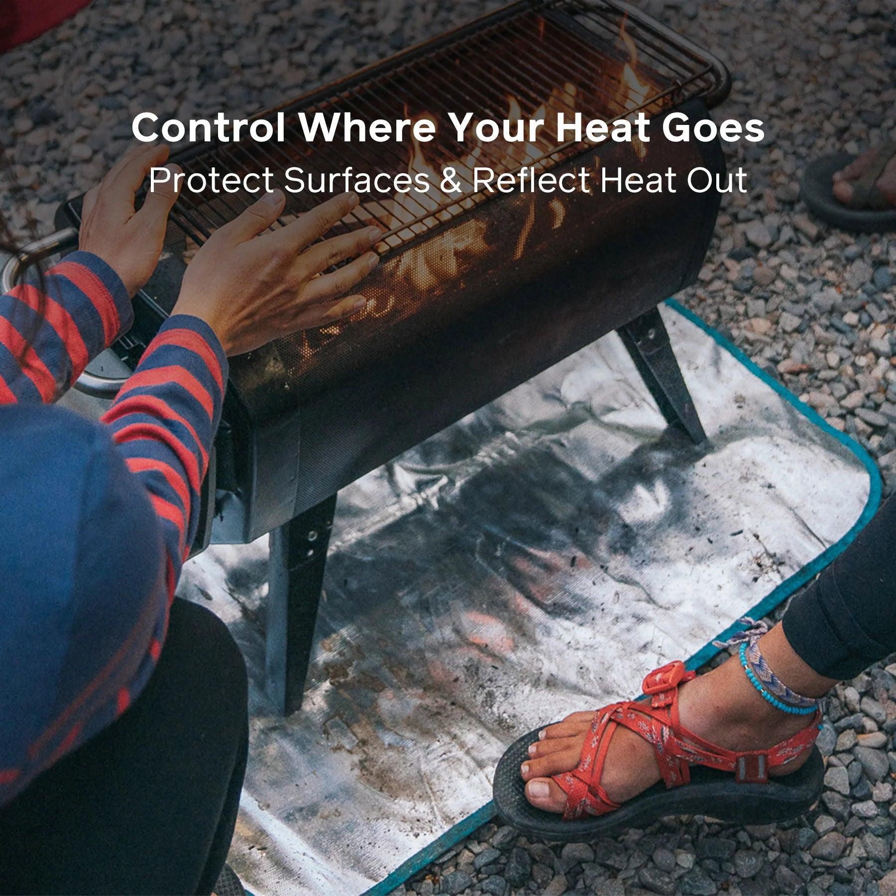 Hands warming by BioLite FirePit on reflective fire mat outdoors on gravel