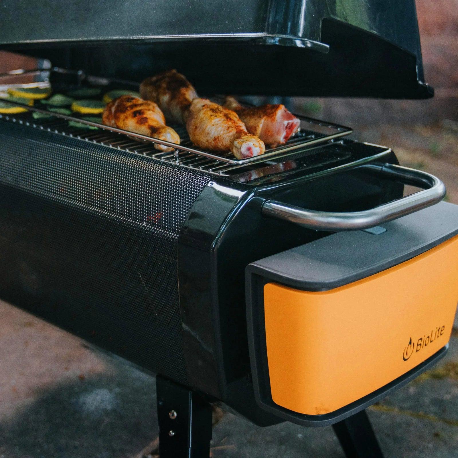 BioLite FirePit outdoor grill with chicken drumsticks and vegetables cooking under open lid
