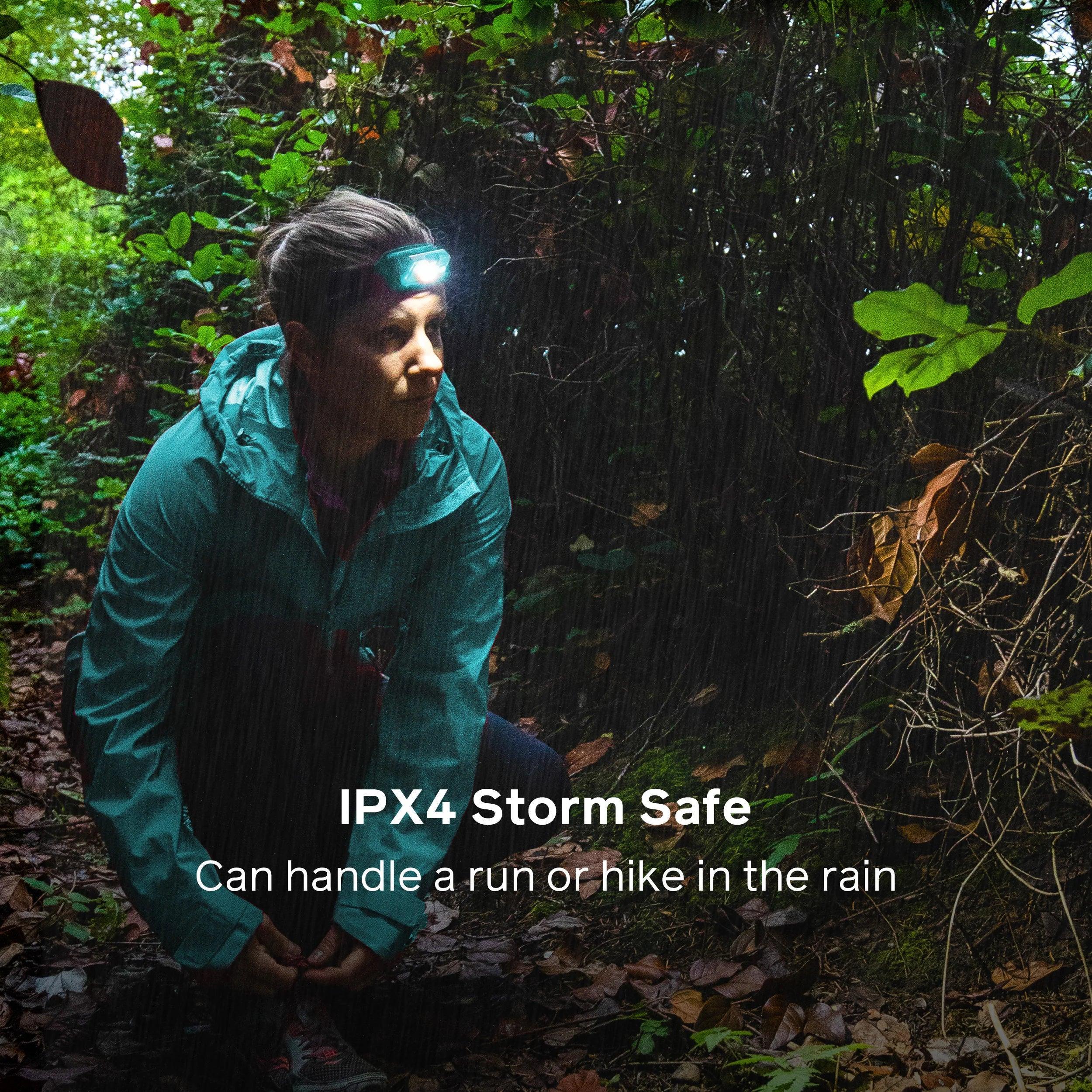 Woman wearing BioLite headlamp hiking in rain in forest, IPX4 storm safe outdoor gear