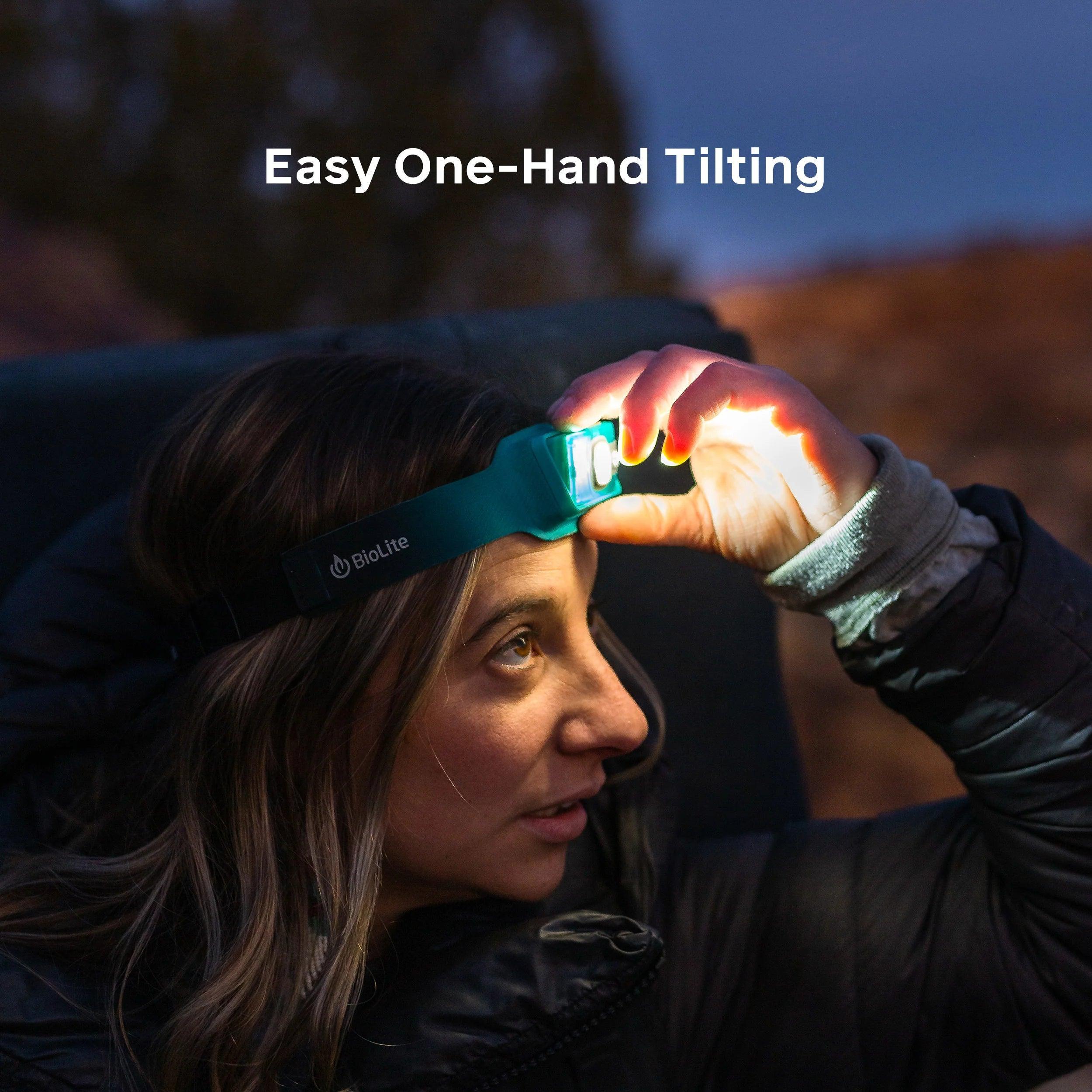 Woman outdoors tilting teal BioLite headlamp with one hand at dusk