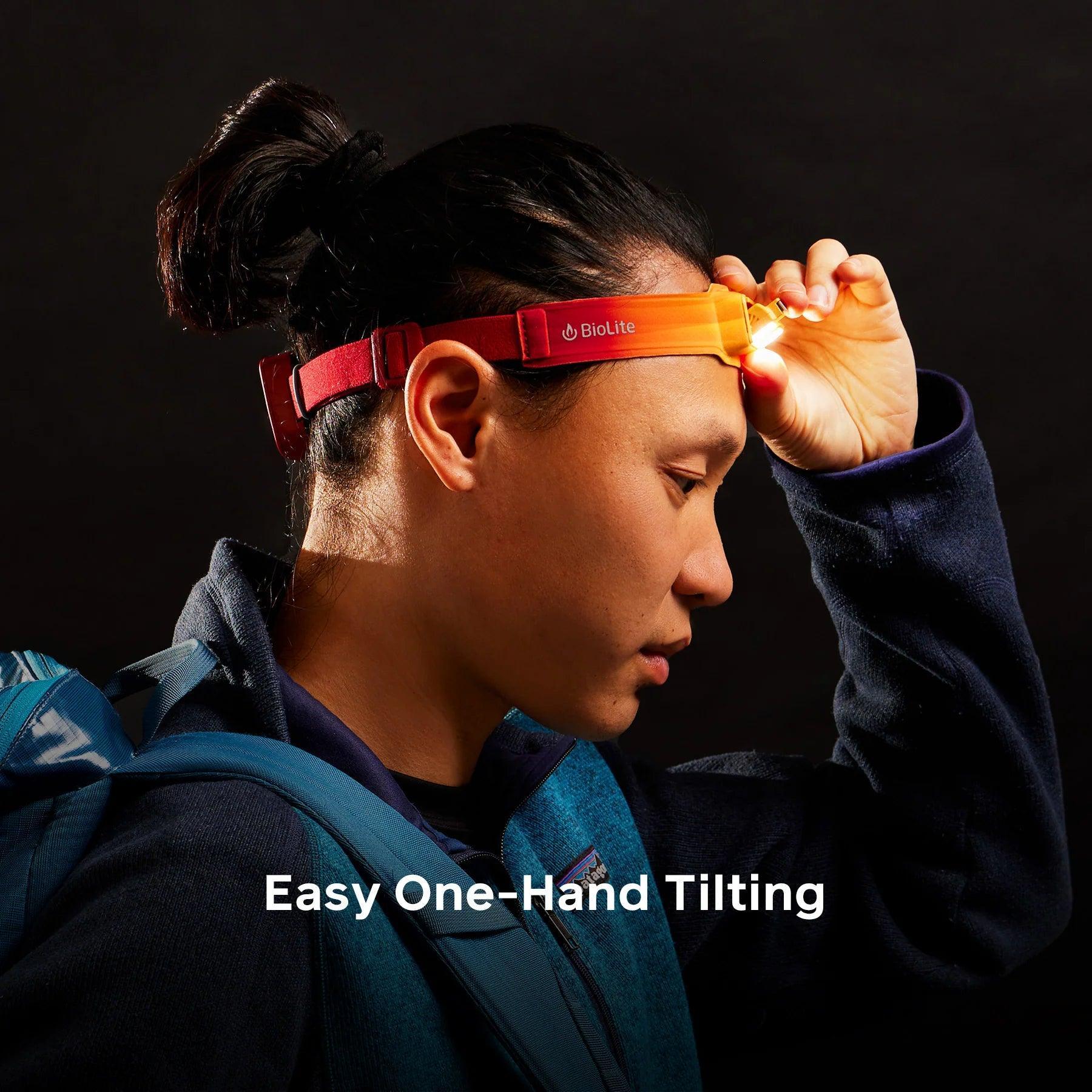 Person adjusting BioLite HeadLamp 425 with one hand, wearing outdoor backpack, dark background