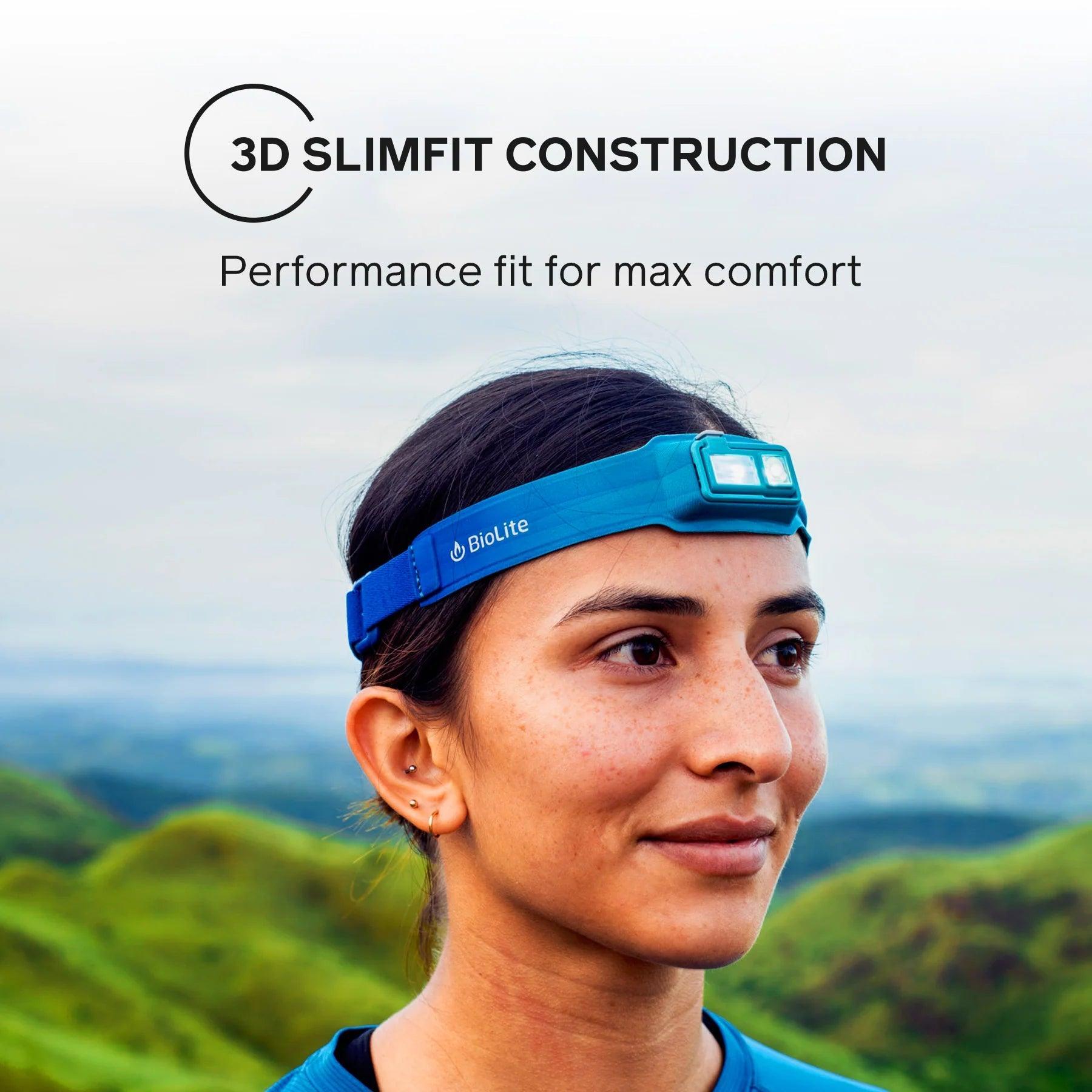 Woman wearing BioLite blue headlamp outdoors with green hills in background