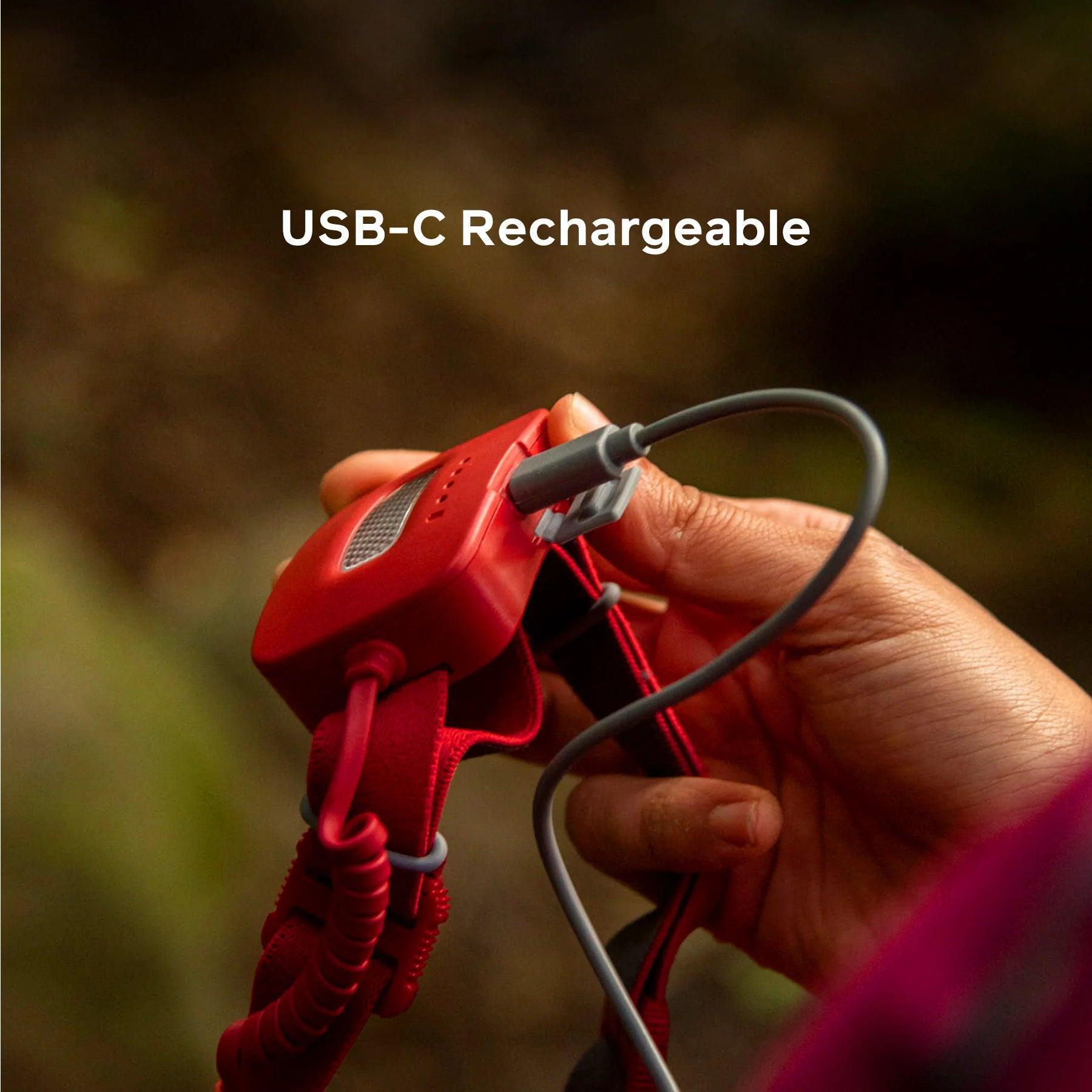 Hand charging red BioLite headlamp with USB-C cable outdoors