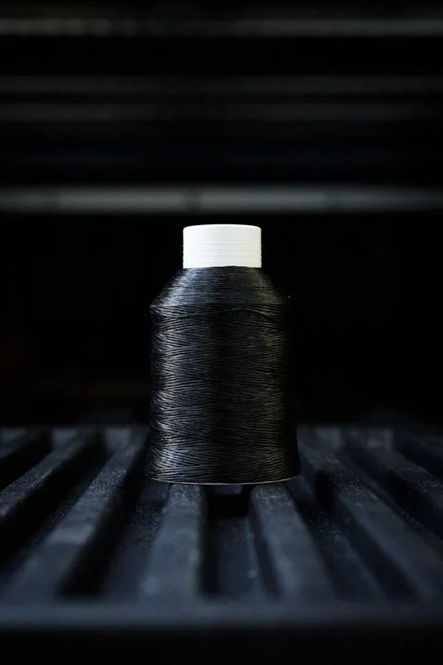Black thread spool with white top on dark textured surface, industrial background