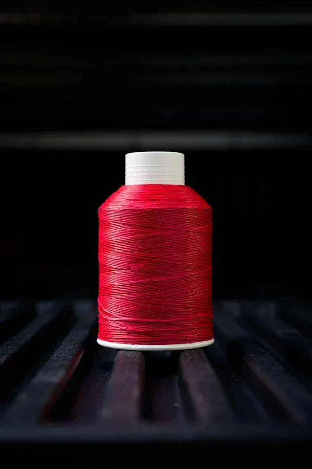 Sunset red thread spool with white cap on a dark textured surface, close-up sewing supply.