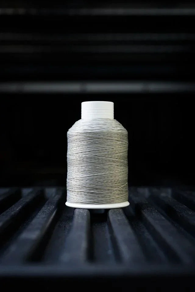 Stone grey sewing thread spool on dark textured surface, close-up product photo