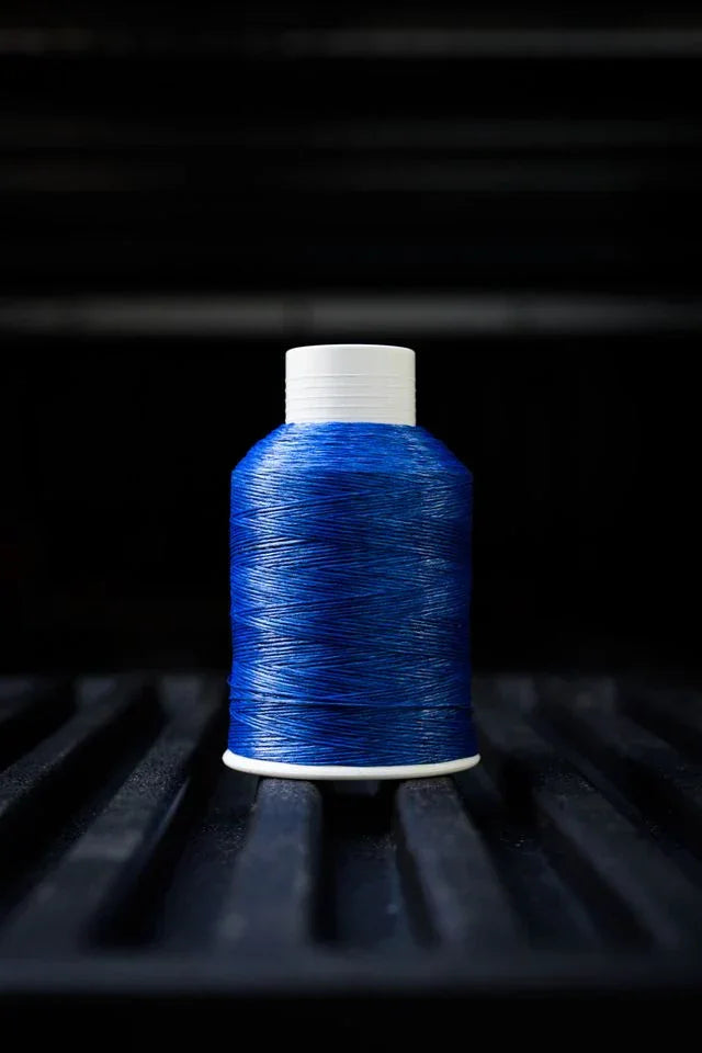 Royal blue thread spool with white cap on black textured surface, sewing supplies photography