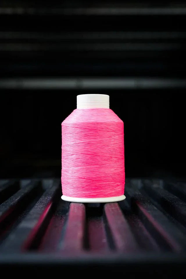 Bright pink thread spool with white cap on black ribbed surface, sewing supplies
