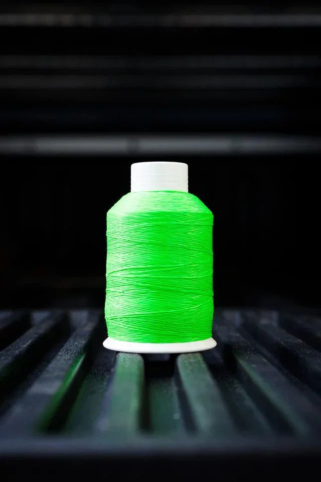 Bright green thread spool with white cap on black grooved surface