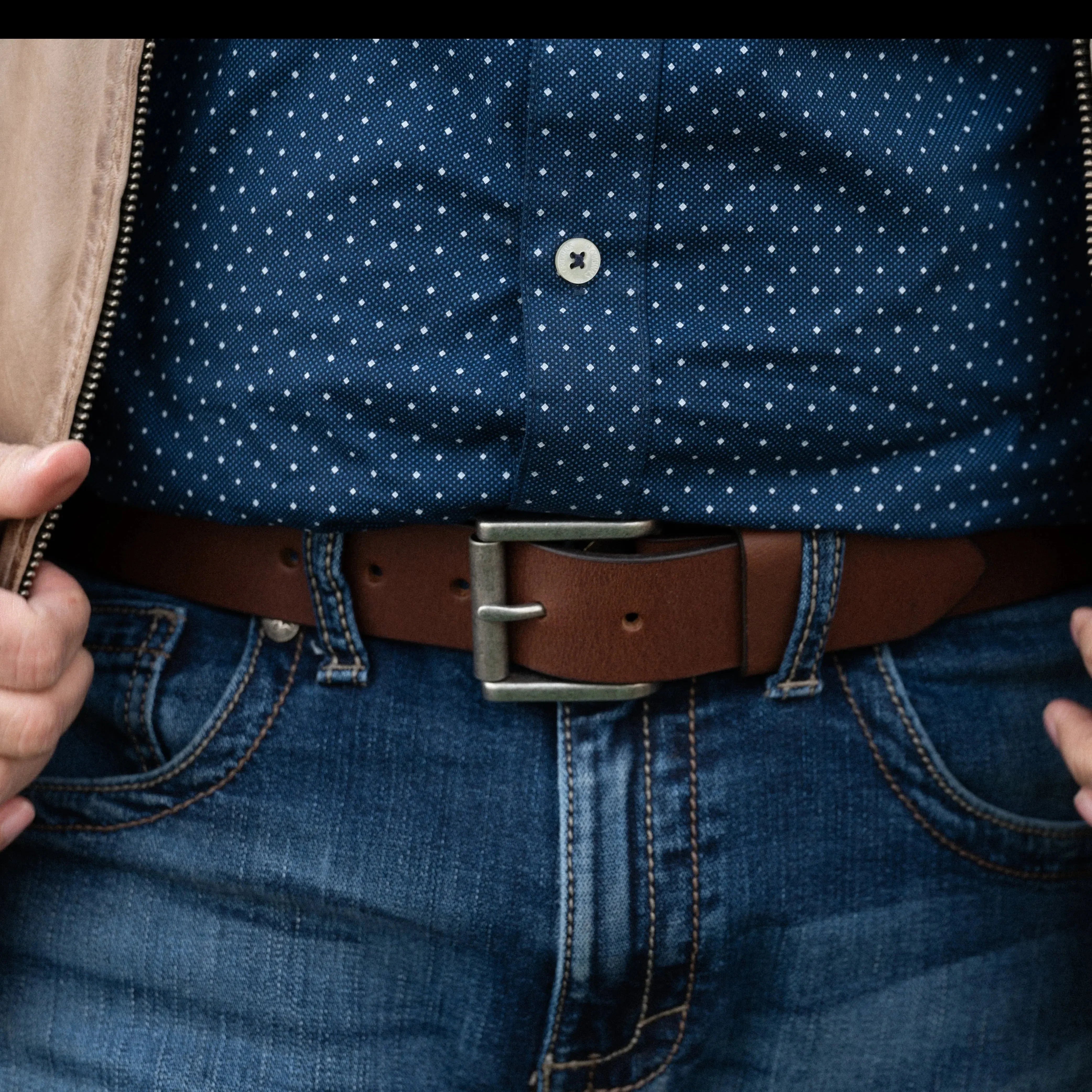 Brown men's leather belt with removable buckle on jeans and blue polka dot shirt