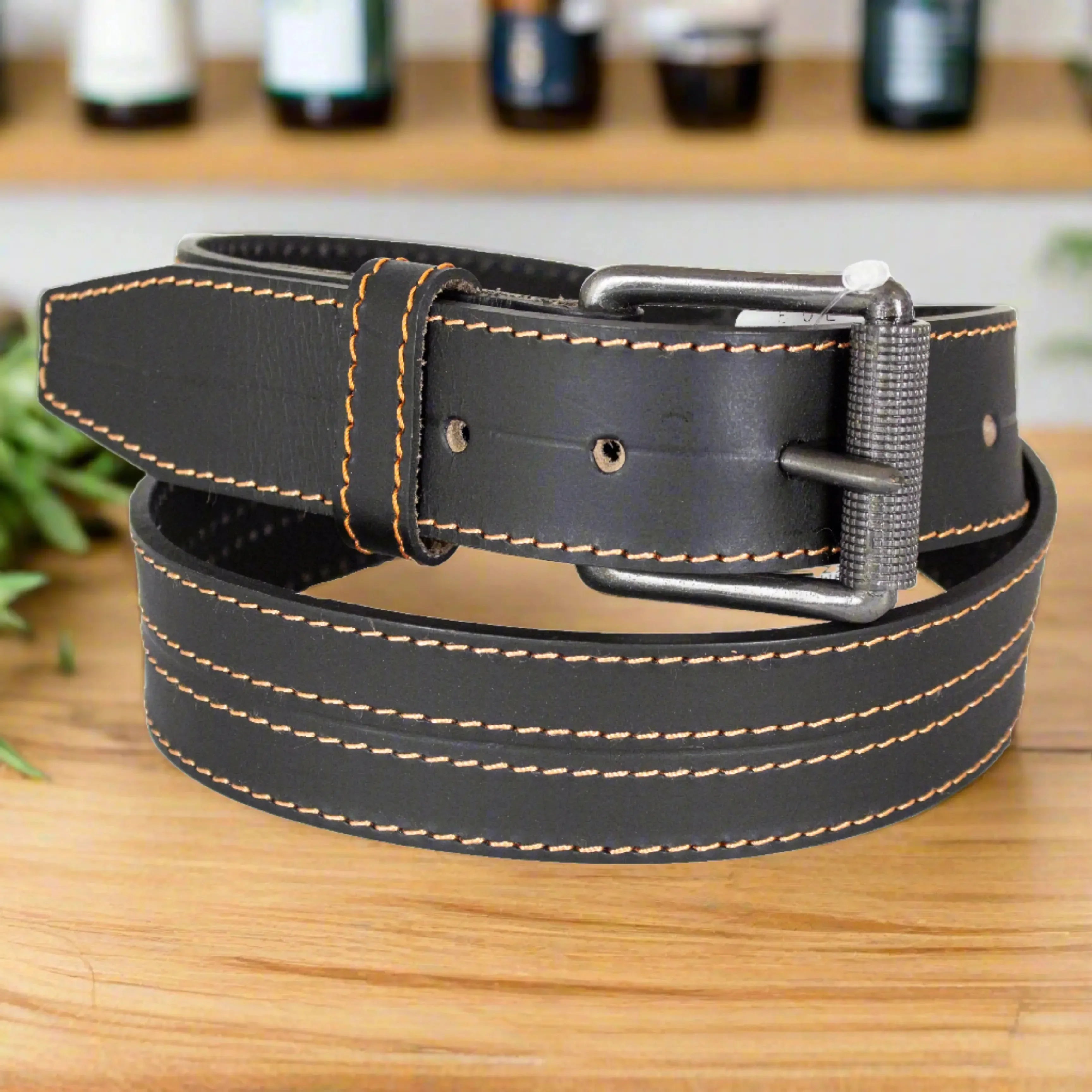Men's black leather belt with roller buckle and orange stitch detail on wooden table