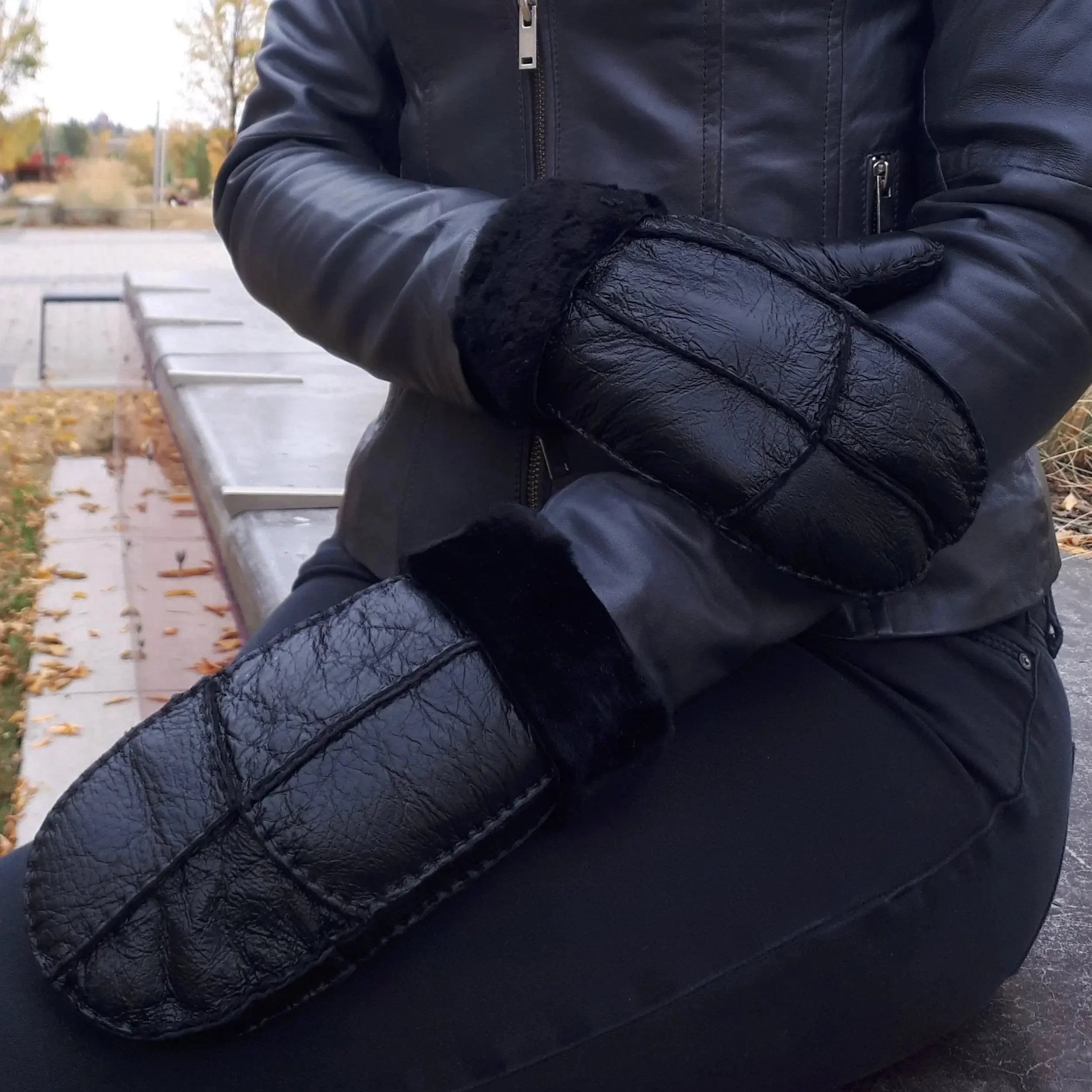 Man wearing black shearling leather mittens and jacket outdoors in autumn