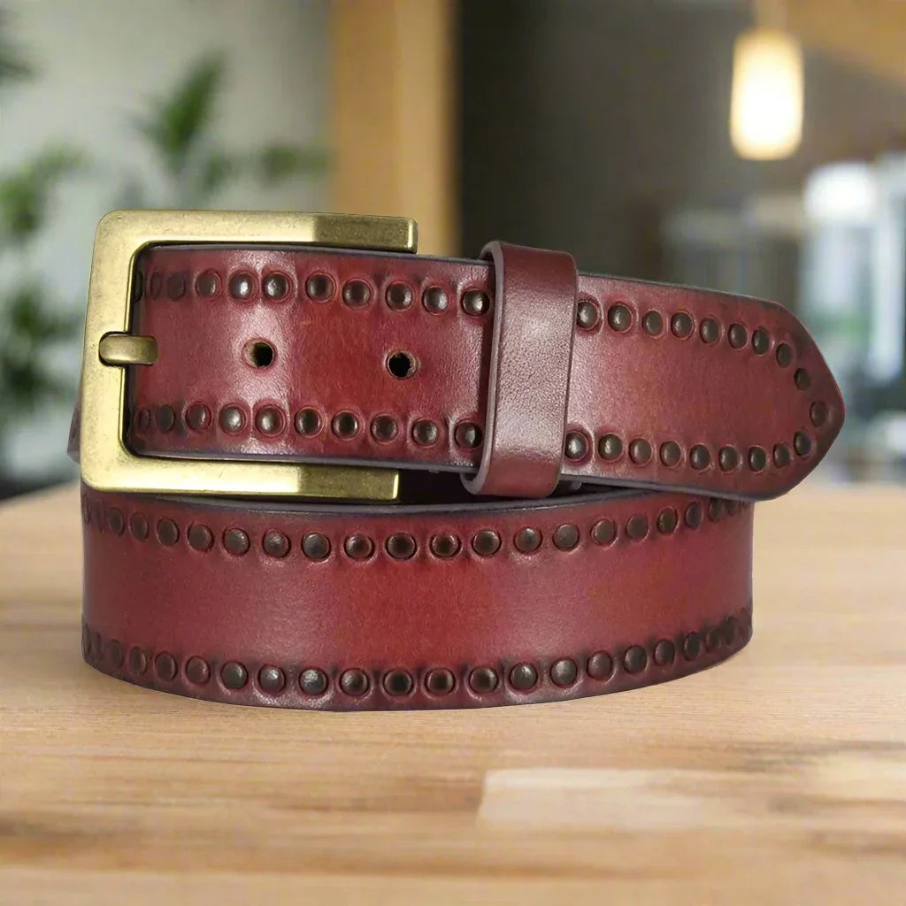 Unisex tooled leather belt with brass buckle and circle detailing on wooden table