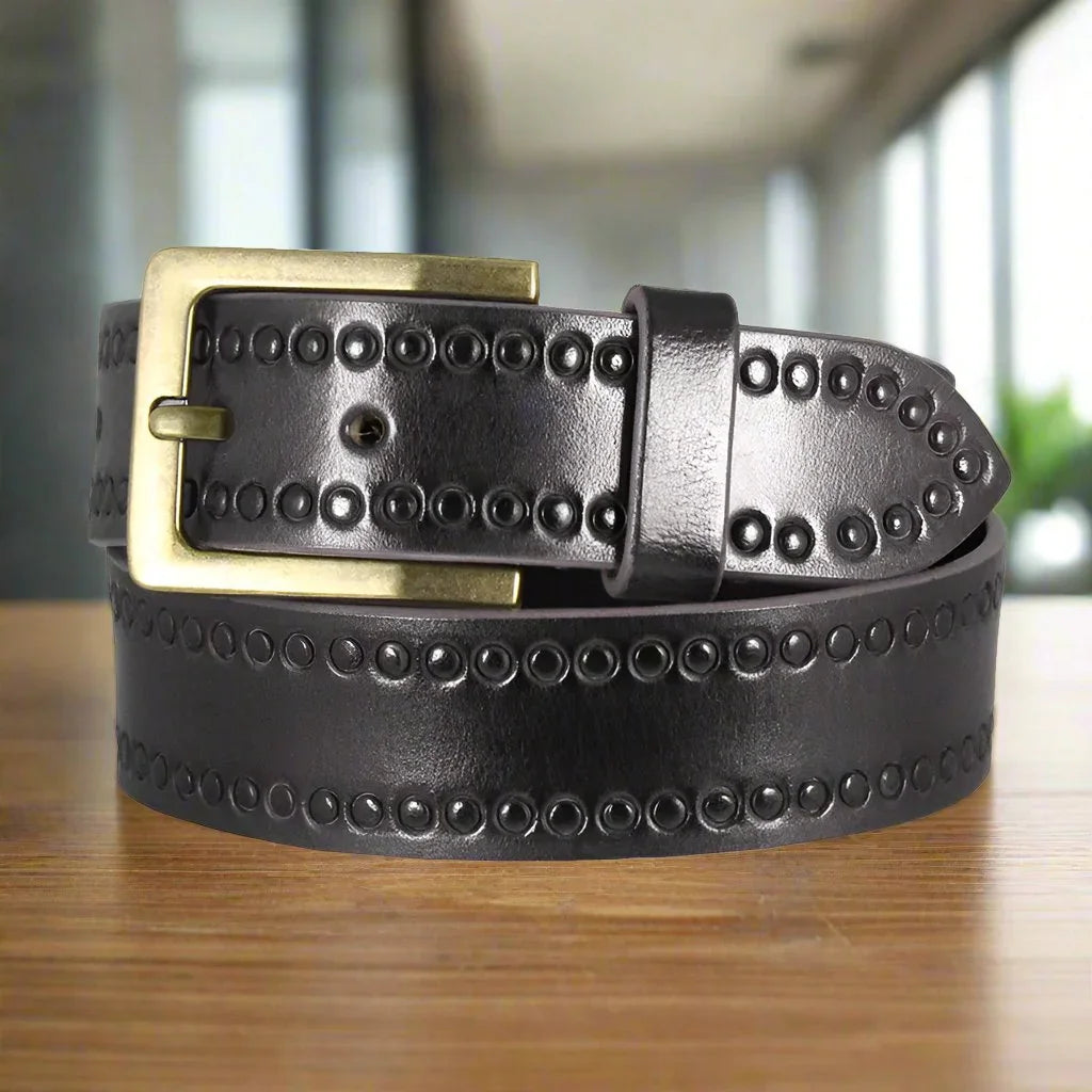 Black tooled leather belt with brass buckle and circular embossing on a wooden surface