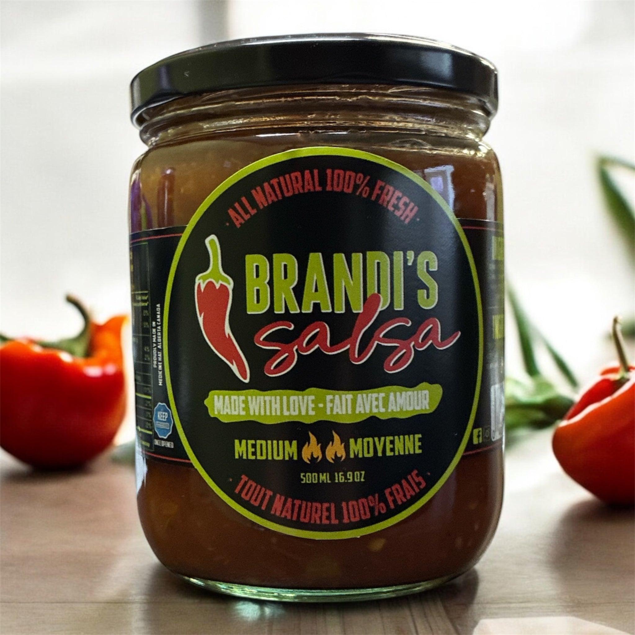 Brandi's Salsa medium jar with fresh red peppers on a wooden table, all natural label visible.