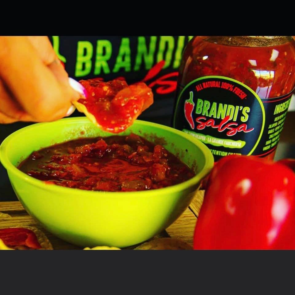 Hand dipping chip in Brandi's Salsa with green bowl and red bell pepper