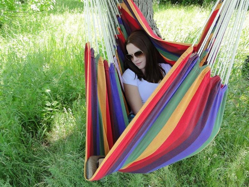 Woman relaxing in a colorful Brazilian hammock chair outdoors on green grass
