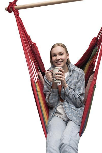 Woman sitting in a colorful Brazilian hammock chair holding a mug, isolated on white background