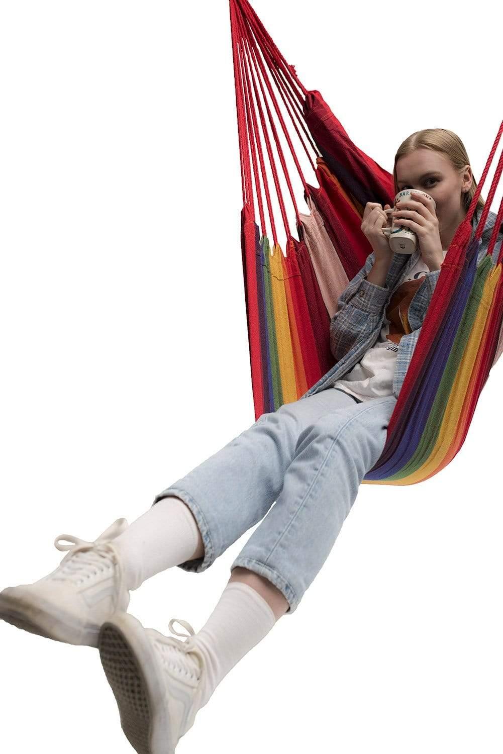 Woman relaxing in a colorful Brazilian hammock chair, holding a mug