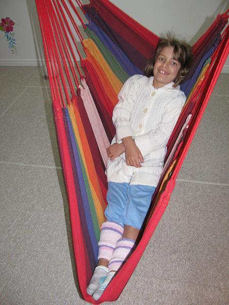 Child lounging on a colorful striped Brazilian hammock chair indoors