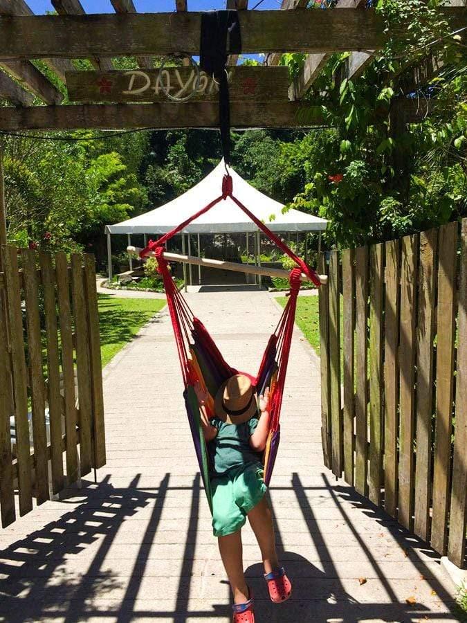 Child relaxing in colorful Brazilian hammock chair outdoors under pergola on sunny day