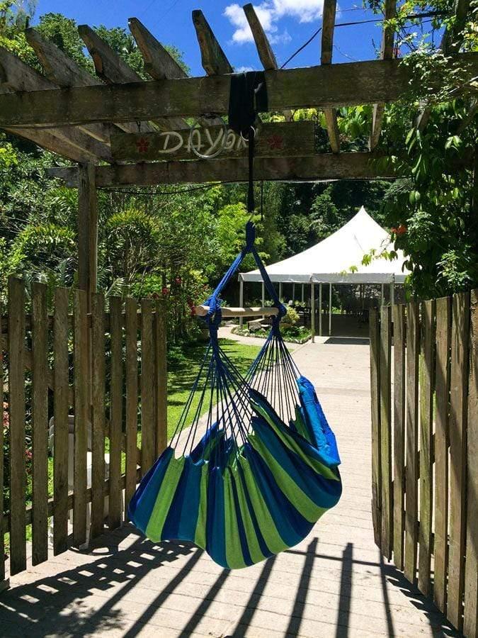 Blue and green Brazilian hammock chair hanging outdoors on a pergola with garden view