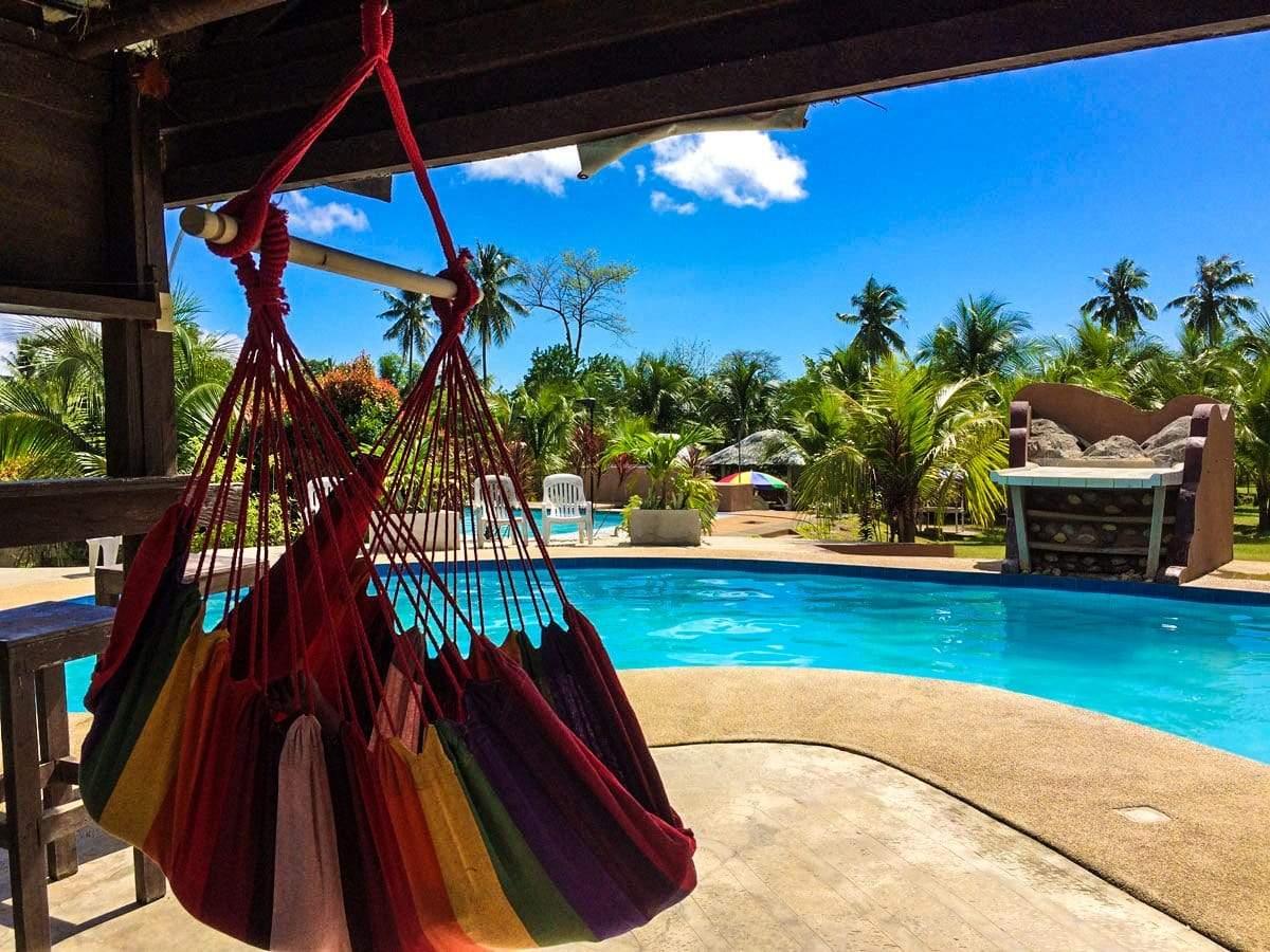 Brazilian hammock chair in hot colors by a tropical outdoor pool with palm trees
