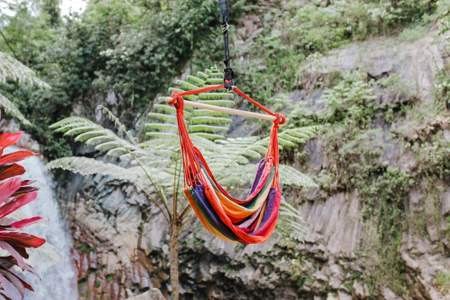 Colorful hammock chair hanging outdoors by lush green waterfall, nature background