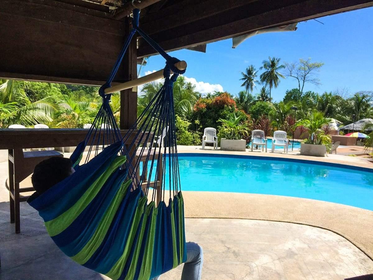 Blue and green Brazilian hammock chair by a tropical poolside under a shaded patio.