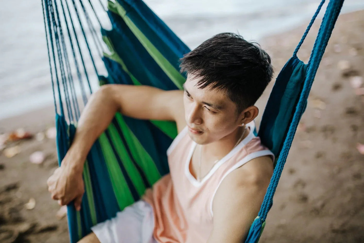 Young man relaxing in blue hammock on sandy beach
