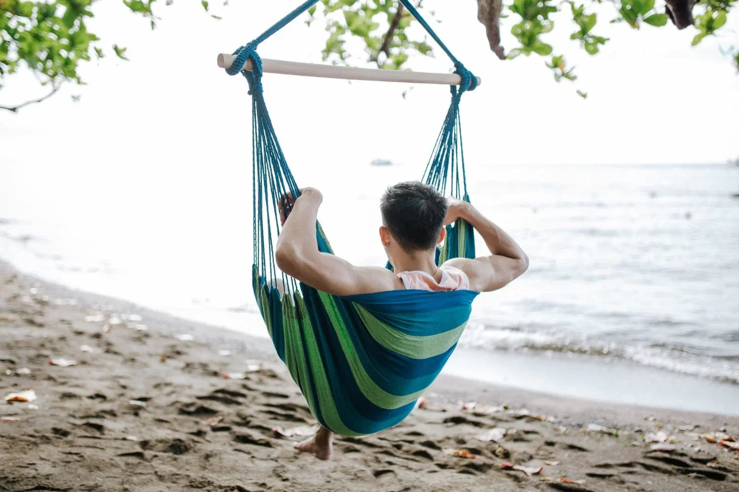 Man relaxing in a blue hammock chair on a tropical beach near the water