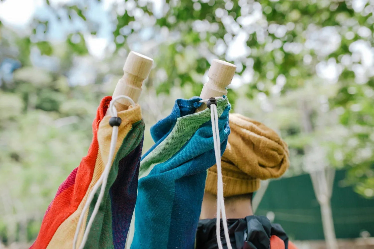 Colorful fabric hammock bags, bamboo handles, outdoor park, person wearing yellow hat