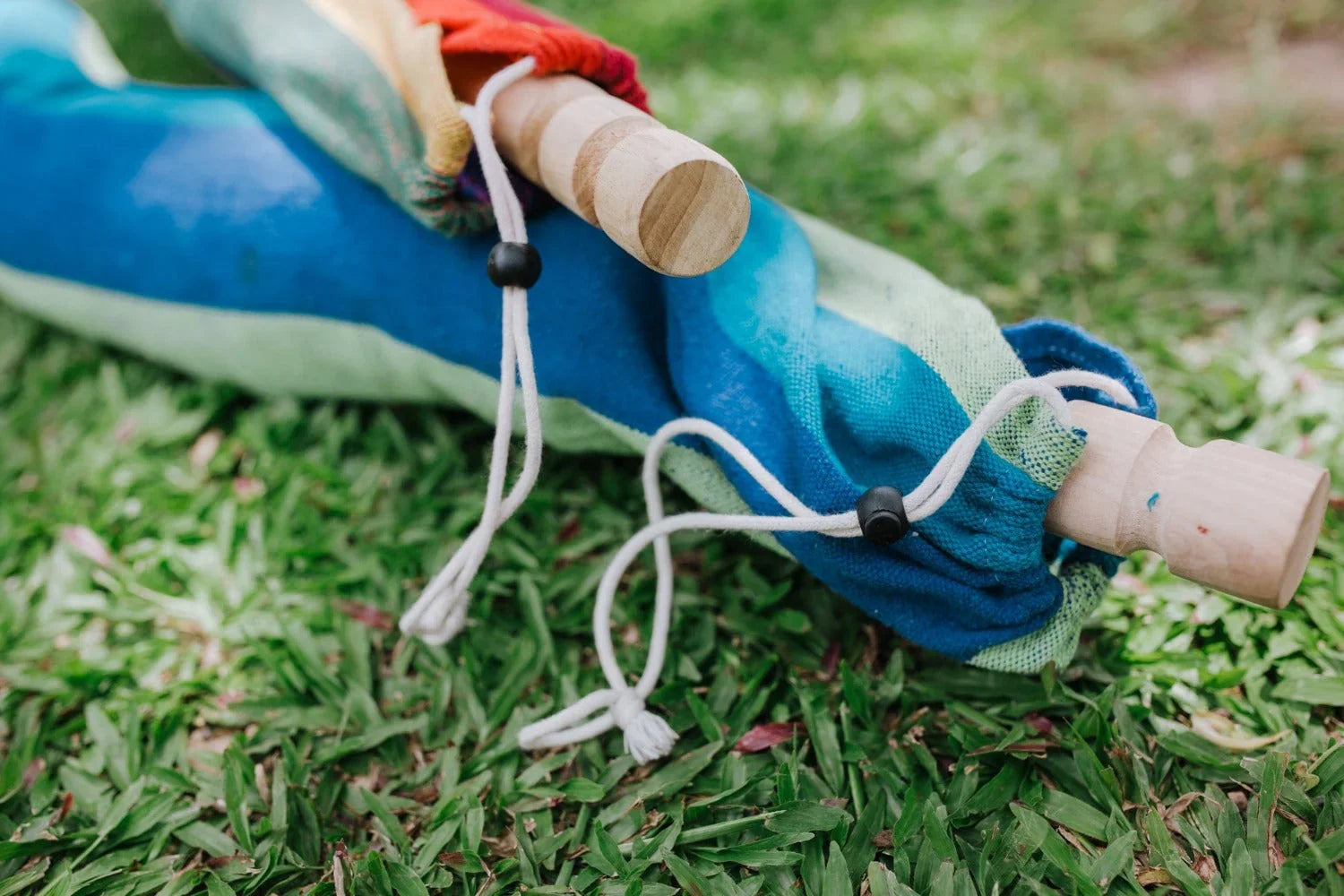 Colorful hammock with wooden ends and drawstrings resting on green grass outdoors