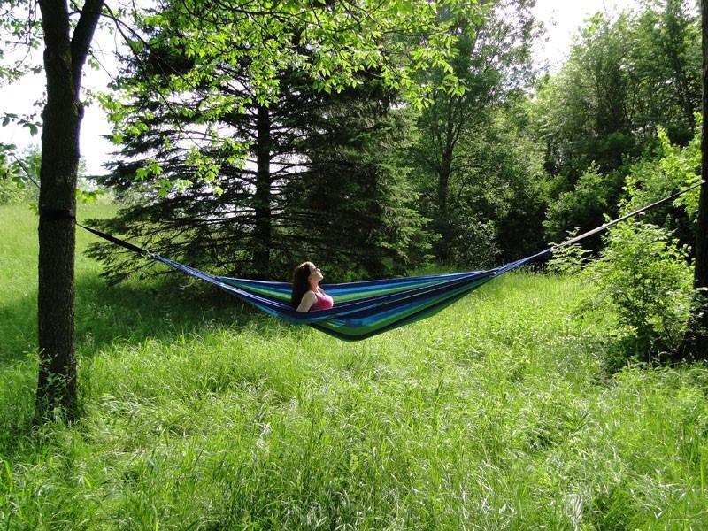 Woman relaxing in a blue striped Brazilian-style hammock in a grassy, wooded area.