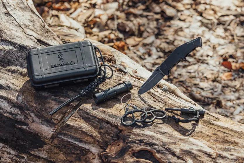 Browning outdoorsman survival kit with knife, case, and tools on a log in the forest