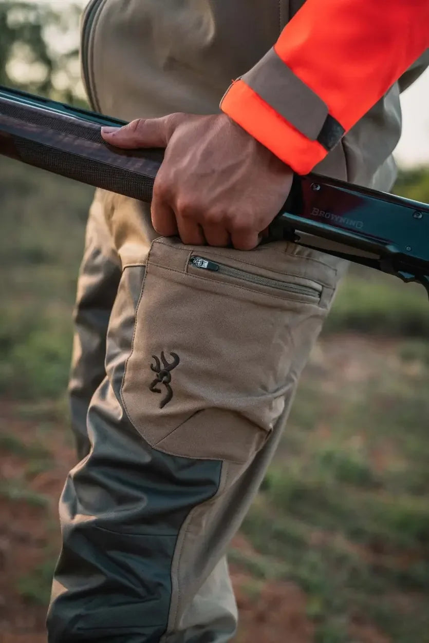Man wearing Browning upland hunting pants and orange jacket holding shotgun outdoors