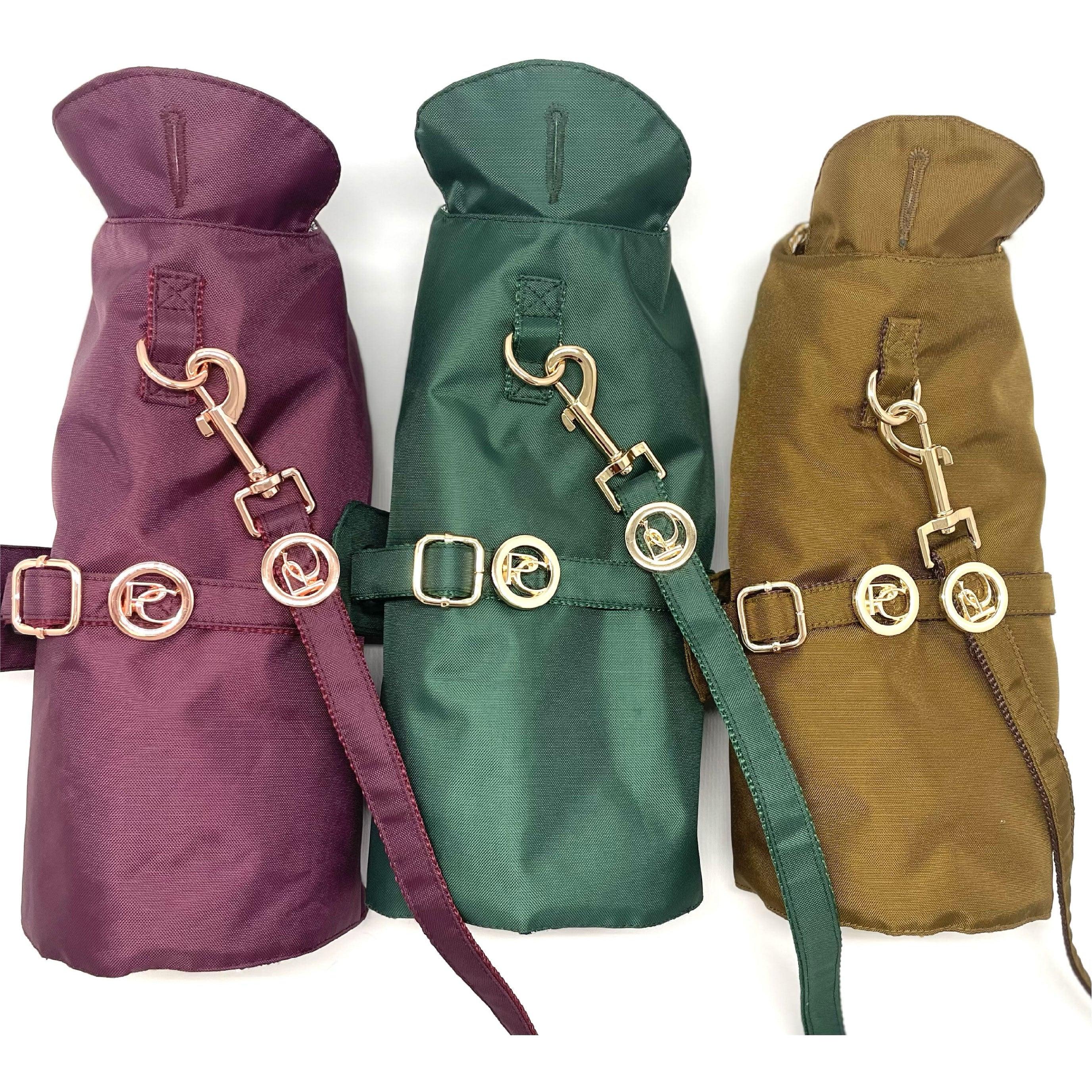 Three dog rain jackets in burgundy, green, and brown with gold hardware, side by side.